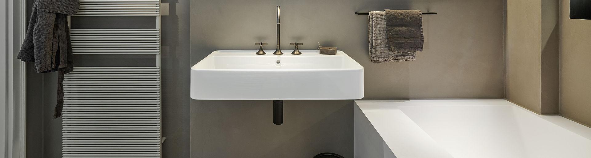 Minimalistisches Badezimmerdesign mit einem rechteckigen Waschbecken, bronzefarbenen Armaturen und dezentem Wandfarbton in Beige.