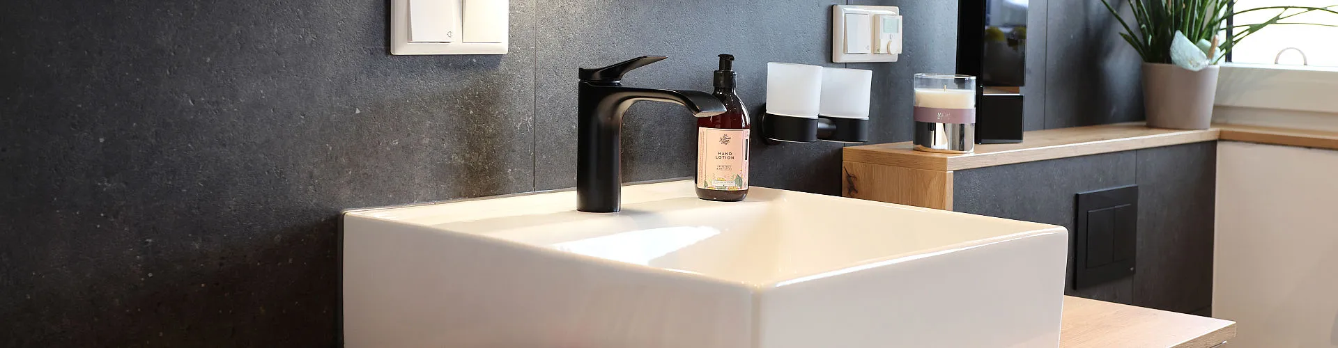 Ein eckiges, modernes Waschbecken mit einer formschönen schwarzen Einhebelarmatur.