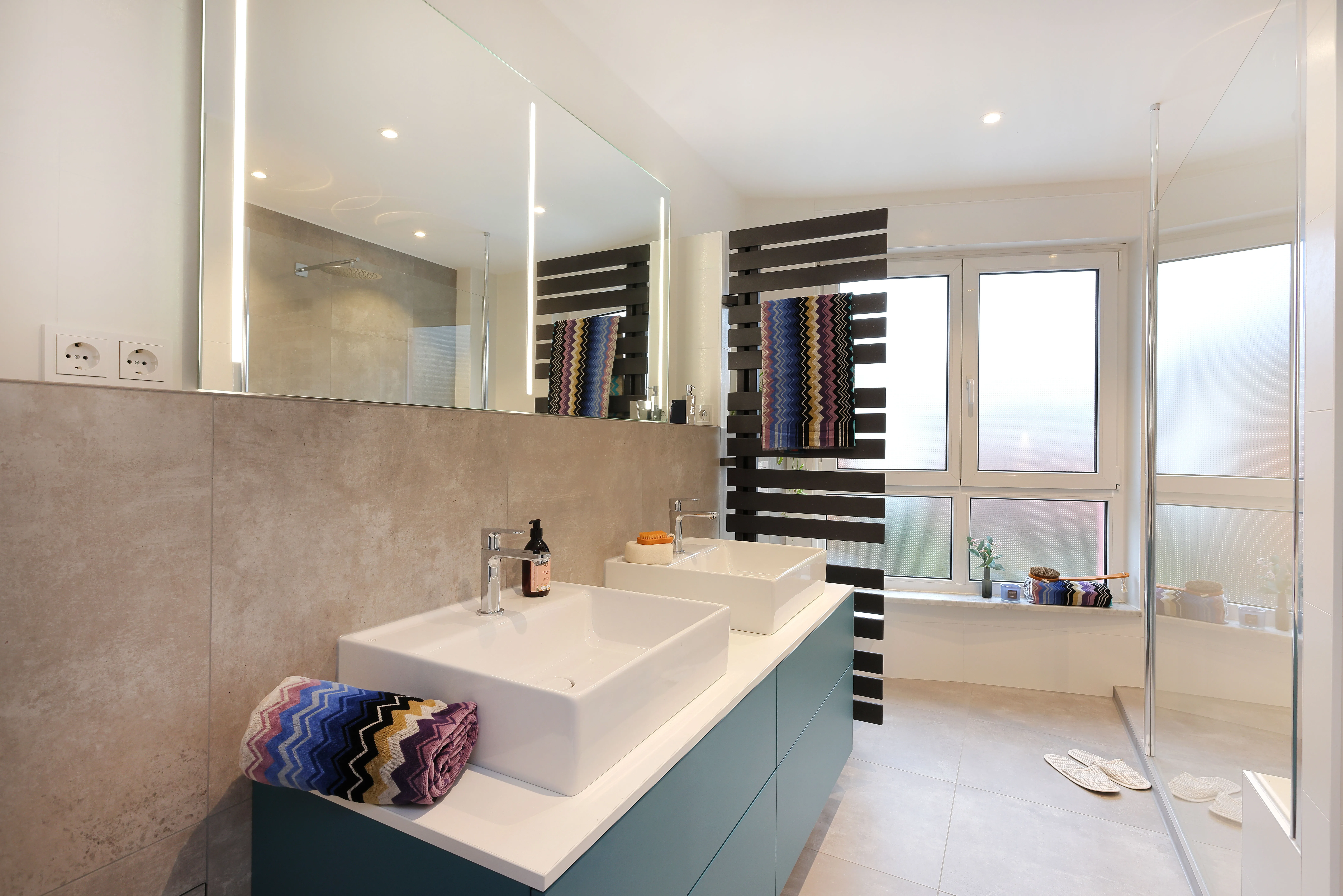 Doppelwaschtisch mit Aufsatzbecken von Burgbad, beleuchtetem Spiegel und farblich abgestimmtem Unterschrank in modernem Bad.