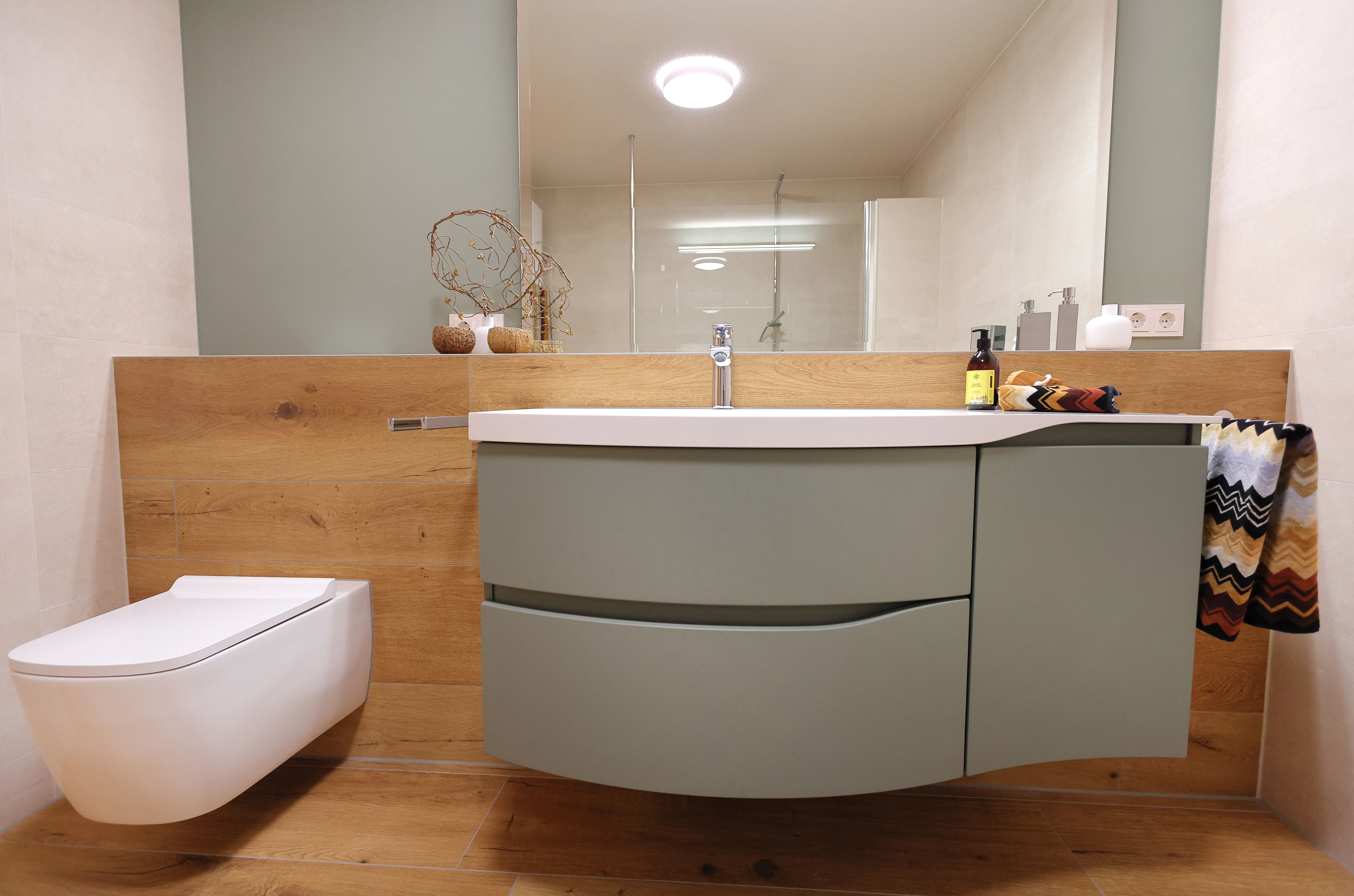 Design-Waschtisch in Salbeigrün mit Holzrückwand und wandhängendem WC in modernem Bad.