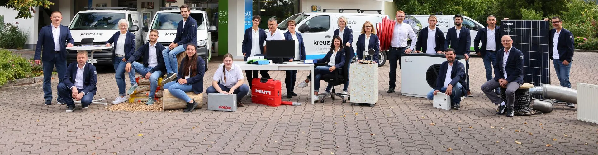 Das gesamte Team der Kreuz bad und heizung gmbh mit Büroequipment, Werkzeugen und Frimenwage vor dem Firmengebäude.