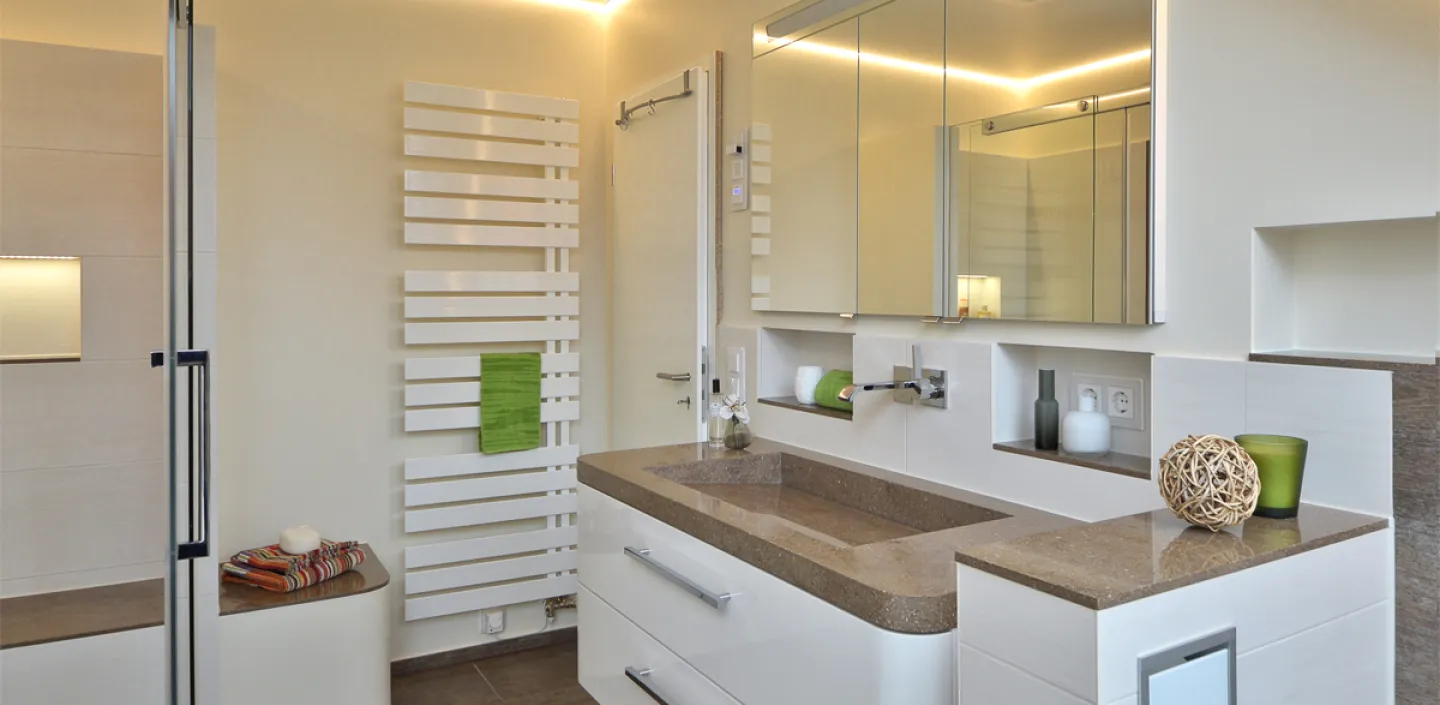 Ein helles Wohnbad mit einem Waschtisch aus Corian, Lichtstreifen an der Decke und grünen Akzenten.