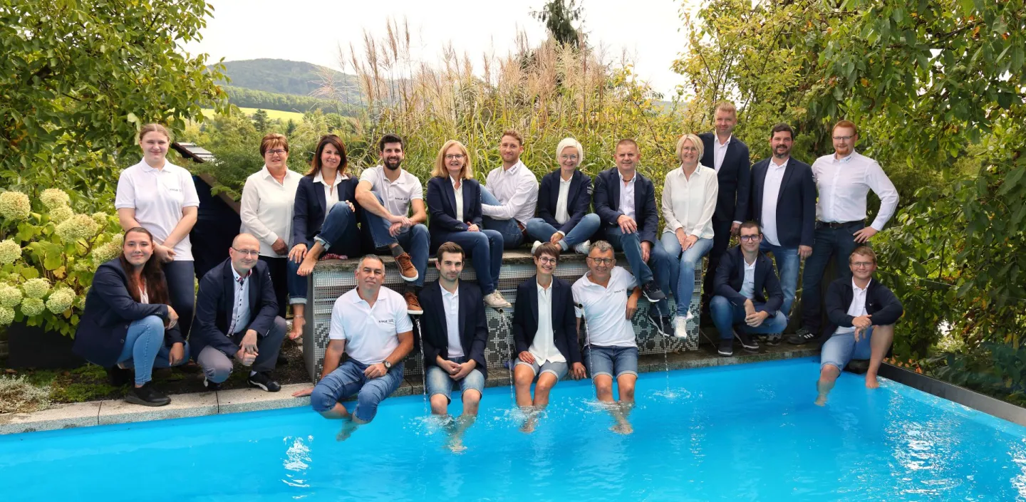 Das gesamte Team der Firma Kreuz bad und heizung aus Schnaittach im Nürnberger Land posiert in feierlicher Kleidung für ein Teamfoto am Rande eines Swimmingpools.
