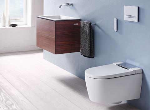 Hellblaues Badezimmer mit Geberit AquaClean Sela Dusch-WC und einem Einbauch-Waschbecken mit Holz-Unterschrank.