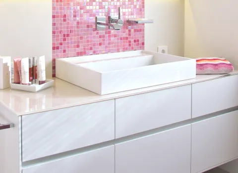 Aufsatz-Waschtisch auf einer Glasplatte mit Unterschrank, betont von einem pinken Glasmosaikstreifen.