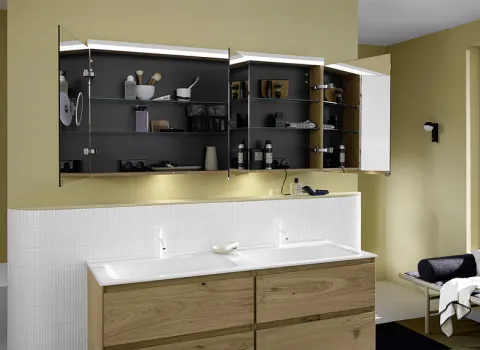 Ein Badezimmer mit einem Doppelwaschtisch aus Holz und drei offenen Spiegelschränken, die diverse Badaccessoires und Pflegeprodukte sichtbar machen.