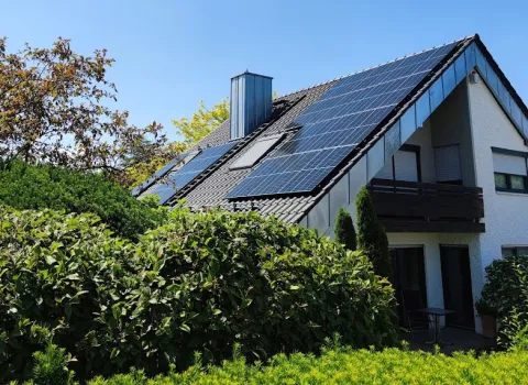Einfamilienhaus mit Solarmodulen auf dem Dach, umgeben von grünem Garten.
