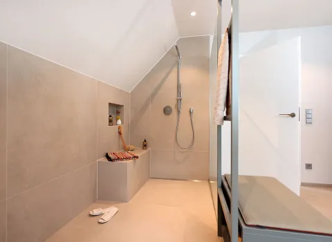 In einem hellen, modern eingerichteten Badezimmer befindet sich eine bodengleiche, offene Dusche mit Regendusche und eingebauter Sitzfläche