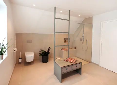 Ein großzügiges Badezimmer unter dem Dach präsentiert eine elegante Walk-in-Dusche mit integrierter Sitzbank und farbenfrohen Handtüchern.