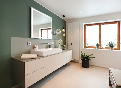 Ein modernes Badezimmer mit grün gestrichener Akzentwand zeigt ein großes, rechteckiges Waschbecken auf einem schwebenden Waschtisch mit mehreren Schubladen.