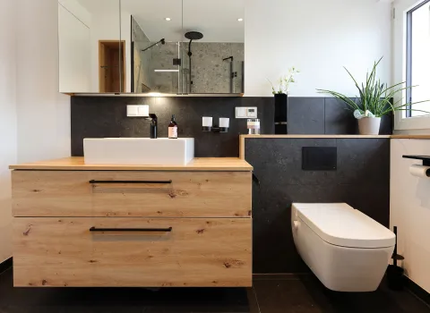 Ein harmonisch gestaltetes Badezimmer kombiniert Holzoptik, schwarze Elemente und weiße Sanitärkeramik zu einem modernen Wohngefühl.