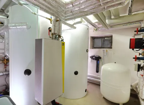 Heizungskeller mit zwei großen Energiespeichern und umfangreicher isolierter Rohrinstallation.
