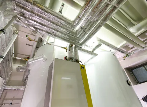 Detailaufnahme der isolierten Heizungsleitungen und Verrohrung im Technikraum.
