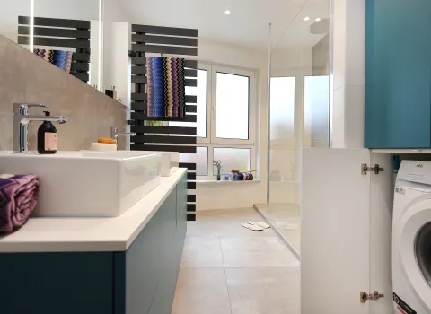 Maßgefertigter Einbauschrank mit integrierter Waschmaschine und Stauraum im modernen Familienbad mit blauen Möbeln.