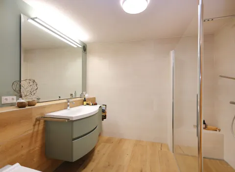 Helles Bad mit großem Spiegel, Holzverkleidung und Walk-in-Dusche mit Glasabtrennung.