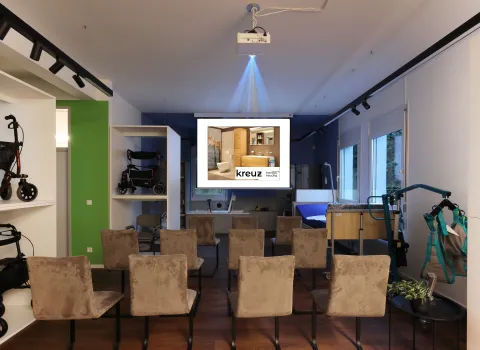 Verkaufsraum mit aufgestellten Stühlen für eine Präsentation, Projektor und Leinwand, im Hintergrund Pflegebett und Reha-Hilfsmittel.