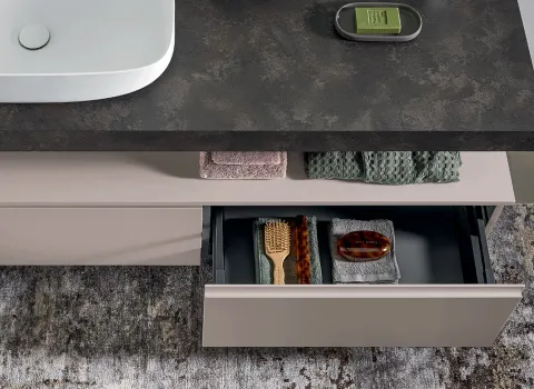 Detailaufnahme eines Stocco Badmöbels mit dunkler Steinplatte, geöffnetem Schubfach und strukturierten Handtüchern.