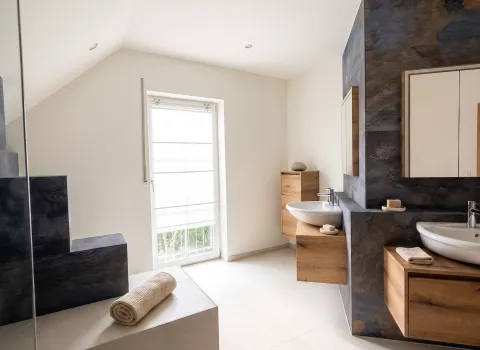 Modernisiertes Badezimmer in Hersbruck mit zwei Waschtischen, Holz-Badmöbeln und großformatigen Wandfliesen.
