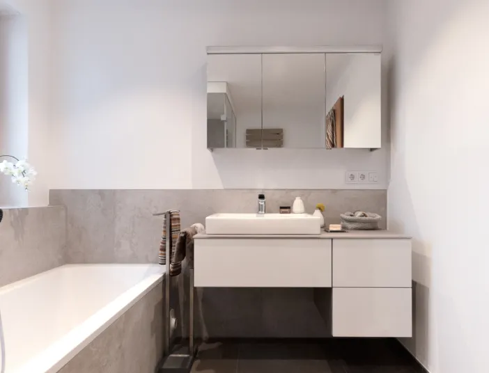 Eine Badewanne und Armatur mit Spiegelschrank in grau und weiß.