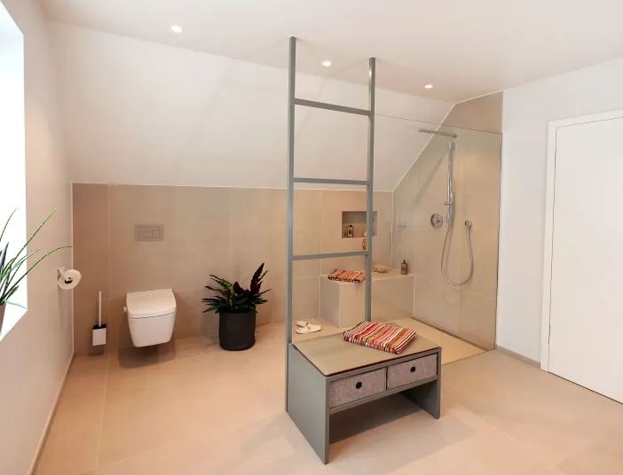 Ein großzügiges Badezimmer unter dem Dach präsentiert eine elegante Walk-in-Dusche mit integrierter Sitzbank und farbenfrohen Handtüchern.