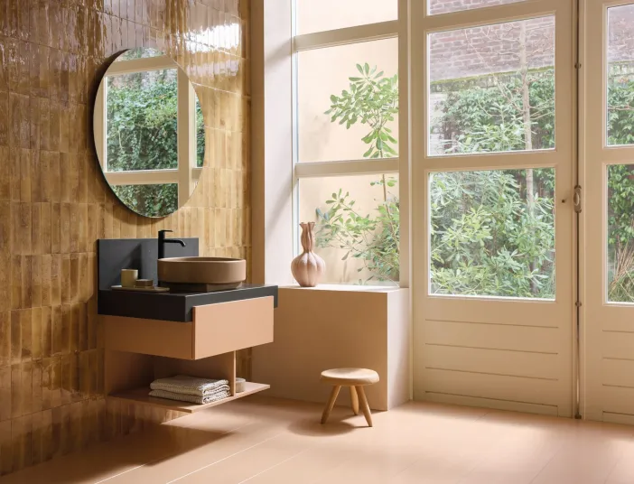 Ockerfarbenes Badezimmer mit einem Premium-Aufsatzwaschbecken der Serie Balcoon von Duravit vor einer großen Tuer- und Fensterfront mit gruenen Pflanzen.